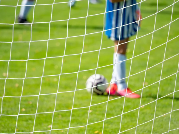 Young football goalkeeper in playground. Out of focus. View through the football gate net.