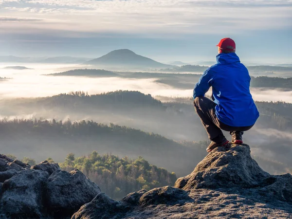 自然冒険だ ハイカーは岩の上に座り 霧の多い朝の谷を眺め 地平線で太陽が昇るのを見る — ストック写真