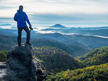 Kamera, kayanın üzerinde duran ve manzaraya bakan bir turistin elinde. Sisli ülkenin yukarısındaki bir adamın elinde fotoğrafçı ve kamera 