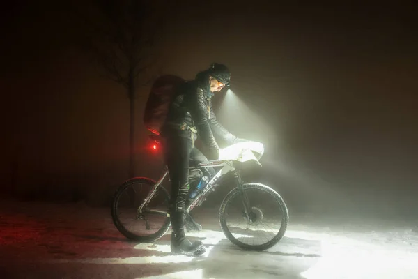 这位身强体壮的运动员站在白雪亮的山地车上 一边在地图上控制着自己的位置 一边进行着极端的定向竞赛 骑自行车的人完全有能力在极端恶劣的天气下比赛 — 图库照片