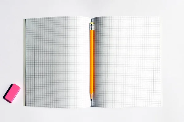 Top view photo of a notebook with checkered pages, with a yellow pencil and a pink eraser lying on it. Study, writing instruments concept.