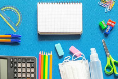 Okul malzemeleri çerçeveli, parlak mavi arkaplanlı boş çizgili kağıt defter. Okul konseptine geri dönelim. Boşluğu kopyala. Sancak. Reklam..