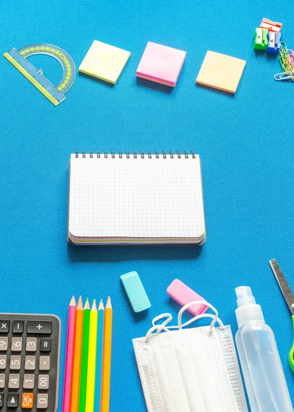 Blank graphing paper notebook with school supplies frame against a bright blue background. Back to school concept. Copy space.banner.advertisement.