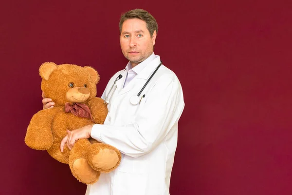Kinderarts Een Witte Jas Houdt Een Bruine Teddybeer Rode Achtergrond — Stockfoto