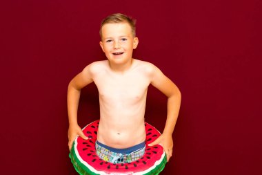 Yaz tatili konsepti, mutlu beyaz çocuk portresi çıplak çocuk şortu karpuz şişirilebilir yüzük yaz tatilinde eğlenen çocuk, kırmızı arka plan..