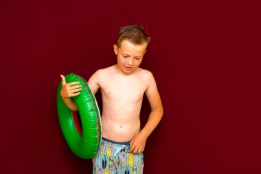 Yaz tatili konsepti, mutlu beyaz çocuk öğrenci portresi çıplak mayo yeşil şişme yüzük yaz tatilinde eğlenen çocuk, kırmızı arka plan..