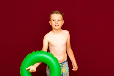 Yaz tatili konsepti, mutlu beyaz çocuk öğrenci portresi çıplak mayo yeşil şişme yüzük yaz tatilinde eğlenen çocuk, kırmızı arka plan..