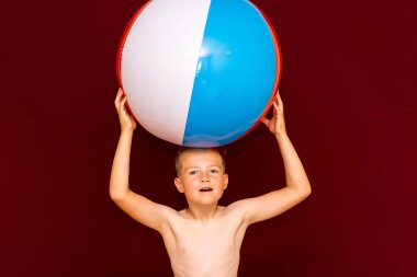 Kırmızı arka planda şişme plaj topu oynayan mutlu beyaz öğrenci. Kafa kafaya top. Yaz tatili kavramı.