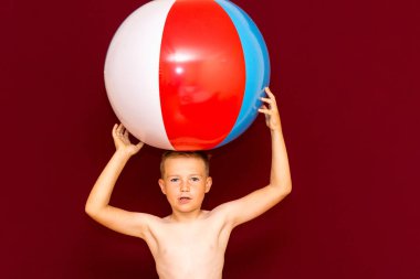 Kırmızı arka planda şişme plaj topu oynayan mutlu beyaz öğrenci. Kafa kafaya top. Yaz tatili kavramı.