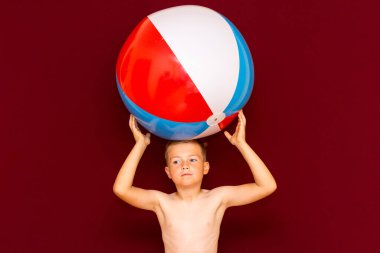 Kırmızı arka planda şişme plaj topu oynayan mutlu beyaz öğrenci. Kafa kafaya top. Yaz tatili kavramı.