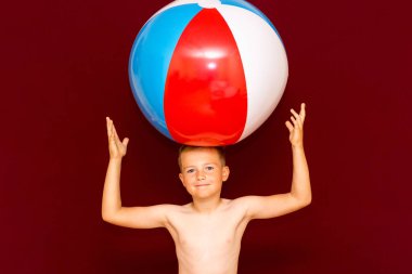Kırmızı arka planda şişme plaj topu oynayan mutlu beyaz öğrenci. Kafa kafaya top. Yaz tatili kavramı.