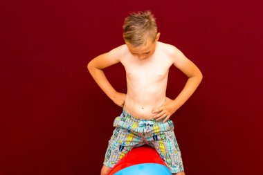 Kafkasyalı mutlu öğrenci kırmızı arka planda şişme plaj topunun üzerine oturur. Yaz tatili kavramı