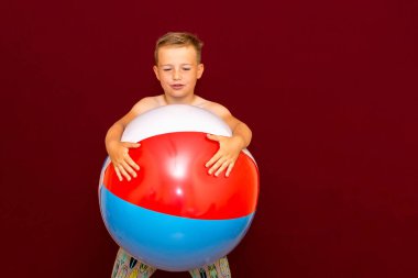 Kırmızı arka planda şişme plaj topu oynayan mutlu beyaz öğrenci. Yaz tatili kavramı