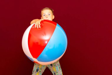 Kırmızı arka planda şişme plaj topu oynayan mutlu beyaz öğrenci. Yaz tatili kavramı