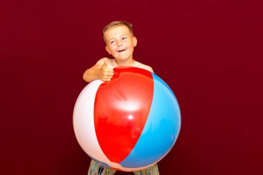 Kırmızı arka planda şişme plaj topu oynayan mutlu beyaz öğrenci. Yaz tatili kavramı