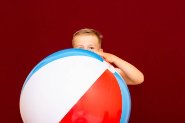 Kırmızı arka planda şişme plaj topu oynayan mutlu beyaz öğrenci. Yaz tatili kavramı