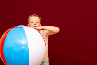 Kırmızı arka planda şişme plaj topu oynayan mutlu beyaz öğrenci. Yaz tatili kavramı