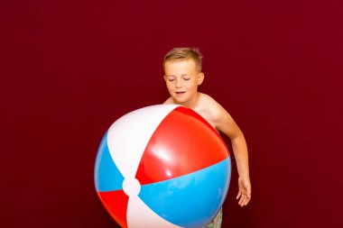 Kırmızı arka planda şişme plaj topu oynayan mutlu beyaz öğrenci. Yaz tatili kavramı