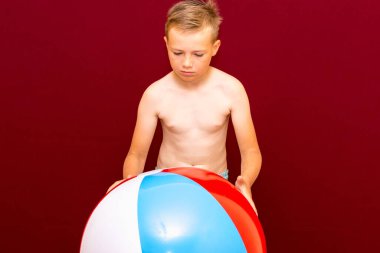 Kırmızı arka planda şişme plaj topu oynayan mutlu beyaz öğrenci. Yaz tatili kavramı