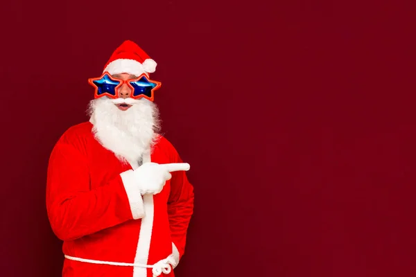 时尚圣诞老人头戴服装手套 头戴星形眼镜 留着白胡子 这些都表明 除了食指外 还有展示横幅促销活动 都是在红色背景下进行的 — 图库照片