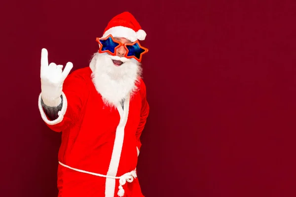派对时间的概念中年喜怒无常的圣诞老人 戴着手套 伸出舌头 在工作室的红色背景上鬼鬼祟祟地嬉笑着 — 图库照片