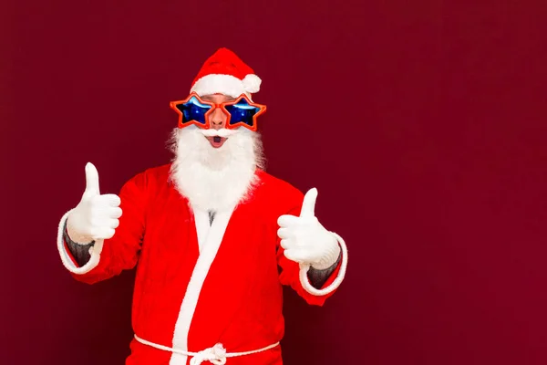 身穿时髦服装的明星眼镜 头戴白色手套的时髦圣诞老人 在红色背景下 在相机前展示自己的成就建议 — 图库照片