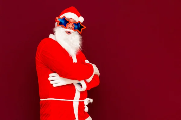 正面年轻圣诞老人的肖像看着相机红色的工作室背景 并在胸前交叉双手交叉地将文本折叠在一起 — 图库照片