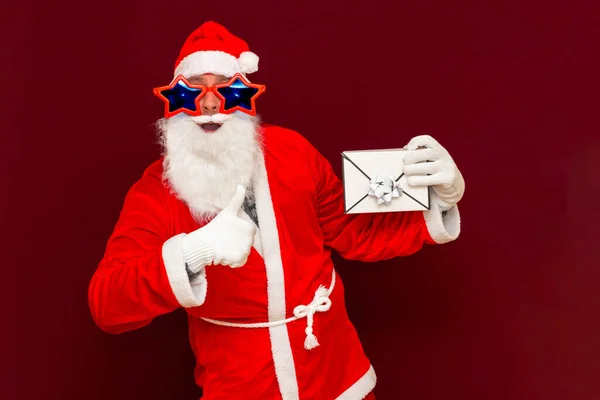 ギフト配送サービス サンタクロースの帽子の偽髭の男はギフトレター封筒ボックスを保持しています クリスマスや新年の休日 人はギフトボックスで示す サンタクリスマス男保持ギフトプレゼント — ストック写真