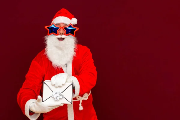 ギフト配送サービス サンタクロースの帽子の偽のひげの男はギフトの手紙の封筒の箱の提示を保持する クリスマスや新年の休日 男のクリスマスのギフトボックス サンタクリスマスの男は贈り物を保持 — ストック写真