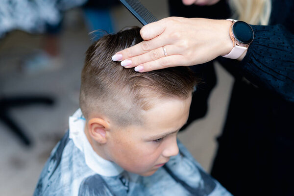 Side view Close up of caucasian american pretty school boy had a trendy haircut with hair clipper at bright modern barbershop.