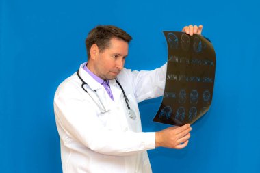 Mavi arka planda beyin tomografisine bakan, düşünceli, Kafkas nöroloji doktoru. Genç bir doktor tarafından incelenen beyin tasviri..