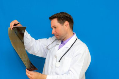 Mavi arka planda beyin tomografisine bakan, düşünceli, Kafkas nöroloji doktoru. Genç bir doktor tarafından incelenen beyin tasviri..