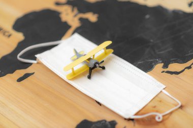 İkinci dalga covid 19 konsept. Oyuncak uçak ve tıbbi koruyucu maske arka plan dünya haritasında. Coronavirüs salgınına bağlı uçuş yasağı kavramı.