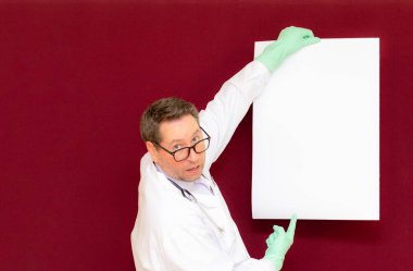 Yetişkin bir doktor portresi, kameraya bakıyor ve boş bir poster tutuyor. Kendi mesaj resminizi eklemek için. Burgundy stüdyo arka planı..