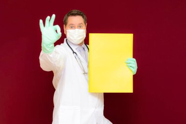 Tıbbi maske takan genç doktor lateks eldiven takıyor ve boynunda sarı boş pankart olan steteskop var. Metin afiş ilanınız için bir yer. Burgundy Stüdyo Duvarı 'nı taklit edin..