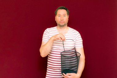 Çizgili tişört giymiş garip bir orta yaşlı adam şarap rengi arka plandaki çöp kutusuna bardak atıyor..