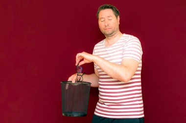 Son moda, çekici, orta yaşlı adam gözlerini kapadı. Çizgili tişört giymiş adam, şarap rengi arka plandaki çöp kutusuna bardak attı..