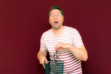 Son moda, çekici, orta yaşlı, çizgili tişört giymiş bir adamın şarap rengi arka plandaki çöp kutusuna bardak atmasına şaşırdım..