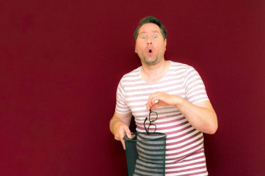 Son moda, çekici, orta yaşlı, çizgili tişört giymiş bir adamın şarap rengi arka plandaki çöp kutusuna bardak atmasına şaşırdım..