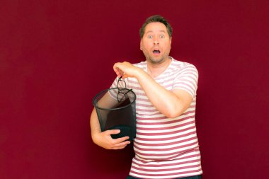 Son moda, çekici, orta yaşlı, çizgili tişört giymiş bir adamın şarap rengi arka plandaki çöp kutusuna bardak atmasına şaşırdım..