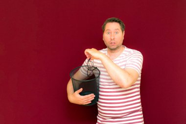 Son moda, çekici, orta yaşlı, çizgili tişört giymiş bir adamın şarap rengi arka plandaki çöp kutusuna bardak atmasına şaşırdım..