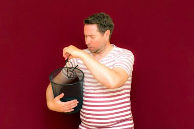 Çizgili tişört giymiş, çöp kutusuna bakıp cam fırlatan modaya uygun, çekici, orta yaşlı bir adam..