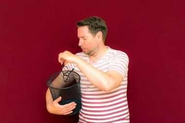 Çizgili tişört giymiş, çöp kutusuna bakıp cam fırlatan modaya uygun, çekici, orta yaşlı bir adam..