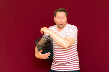 Son moda, çekici, orta yaşlı, çizgili tişört giymiş bir adamın şarap rengi arka plandaki çöp kutusuna bardak atmasına şaşırdım..