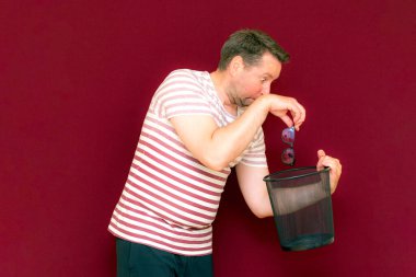 Çizgili tişört giymiş, çöp kutusuna bakıp cam fırlatan modaya uygun, çekici, orta yaşlı bir adam..