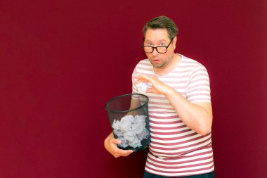 Stripet tişörtlü yakışıklı beyaz adam gözlük takıyor geri dönüşüm kutusunu tutuyor. Bu kağıt atık kağıtlarla çöpe gidecek. Gezegenimizi kurtar. Çöp kutusundaki kağıtların imha edilmesi zorunlu çıktı