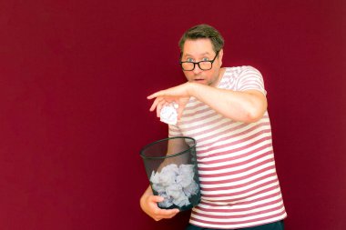 Stripet tişörtlü yakışıklı beyaz adam gözlük takıyor geri dönüşüm kutusunu tutuyor. Bu kağıt atık kağıtlarla çöpe gidecek. Gezegenimizi kurtar. Çöp kutusundaki kağıtların imha edilmesi zorunlu çıktı