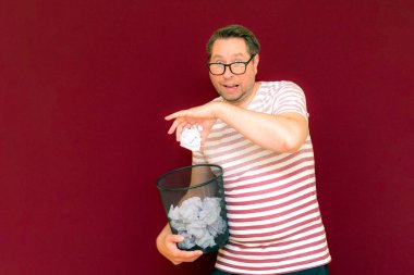 Stripet tişörtlü yakışıklı beyaz adam gözlük takıyor geri dönüşüm kutusunu tutuyor. Bu kağıt atık kağıtlarla çöpe gidecek. Gezegenimizi kurtar. Çöp kutusundaki kağıtların imha edilmesi zorunlu çıktı