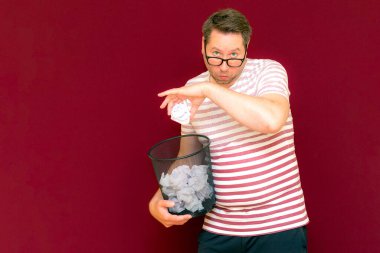 Stripet tişörtlü yakışıklı beyaz adam gözlük takıyor geri dönüşüm kutusunu tutuyor. Bu kağıt atık kağıtlarla çöpe gidecek. Gezegenimizi kurtar. Çöp kutusundaki kağıtların imha edilmesi zorunlu çıktı