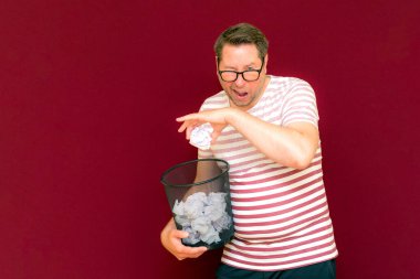 Stripet tişörtlü yakışıklı beyaz adam gözlük takıyor geri dönüşüm kutusunu tutuyor. Bu kağıt atık kağıtlarla çöpe gidecek. Gezegenimizi kurtar. Çöp kutusundaki kağıtların imha edilmesi zorunlu çıktı